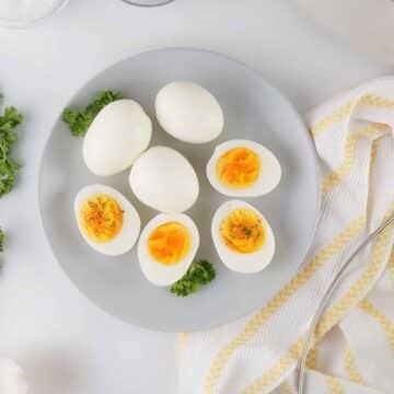 Hard-boiled eggs on a grey plate with two sliced open to show a creamy yolk, garnished with salt, pepper, and fresh parsley.