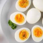 Upclose image of crockpot boiled eggs on a white plate garnished with salt, pepper, and green parsley.