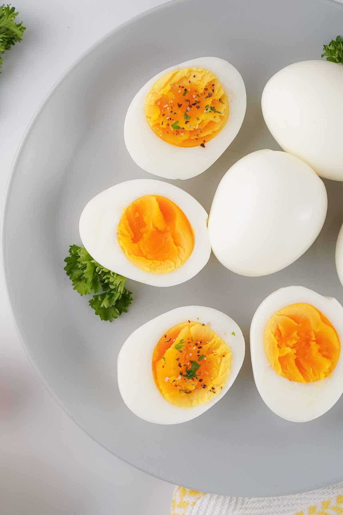 Upclose image of crockpot boiled eggs on a white plate garnished with salt, pepper, and green parsley.