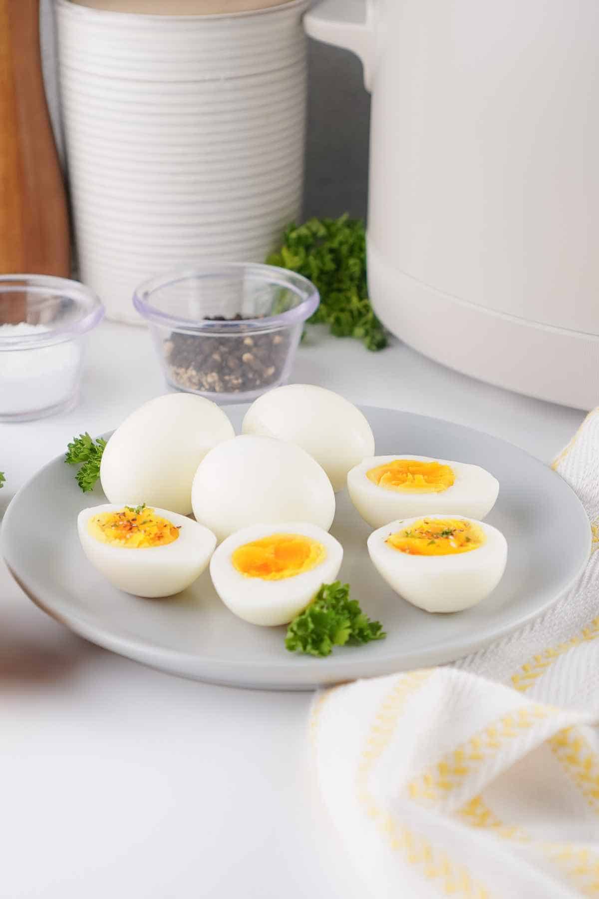 Easy-peel Crockpot boiled eggs sliced in half and served on a plate with a white slow cooker in the background.