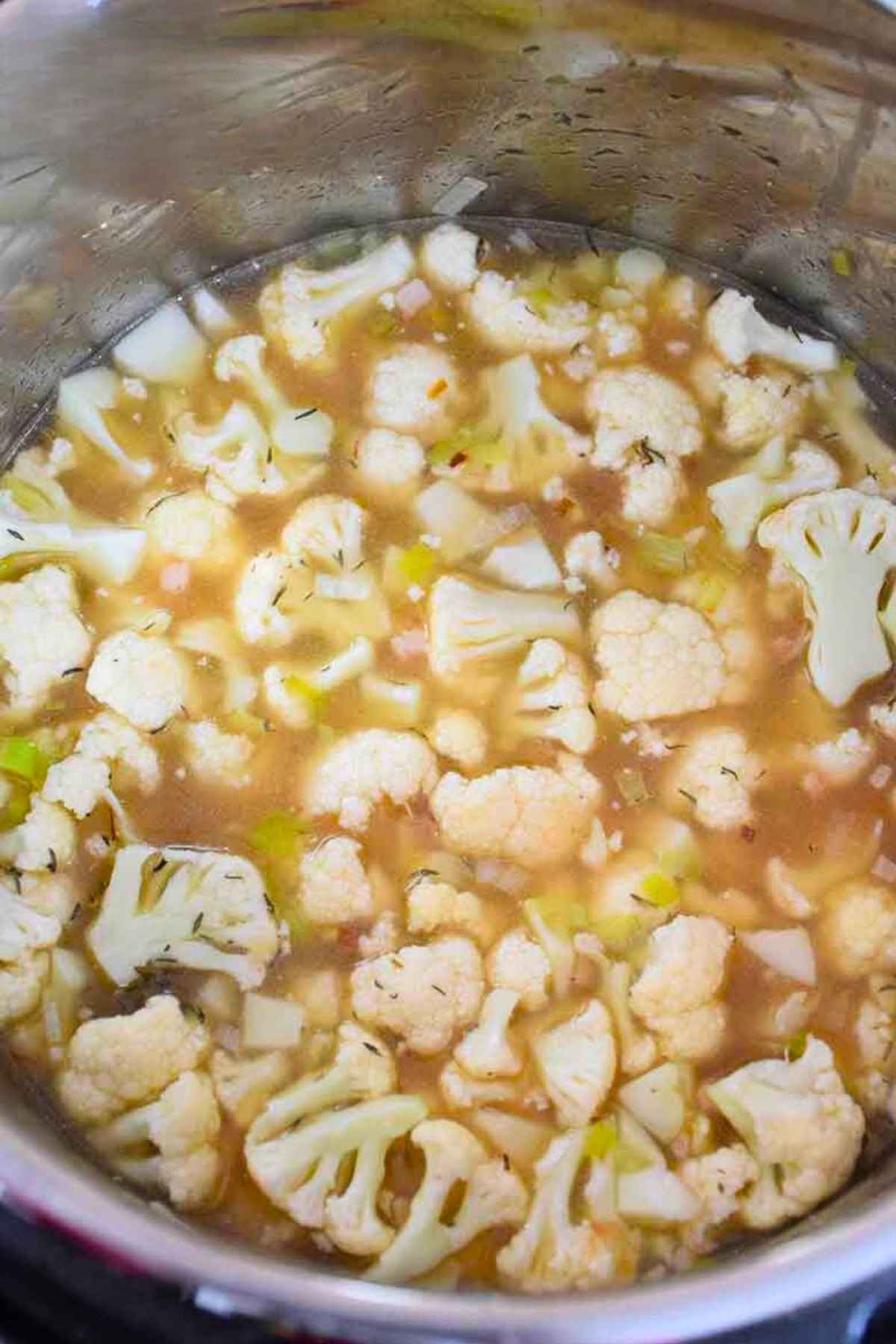 Fresh cauliflower florets, leeks, and pancetta simmering in broth inside a stainless steel Instant Pot.