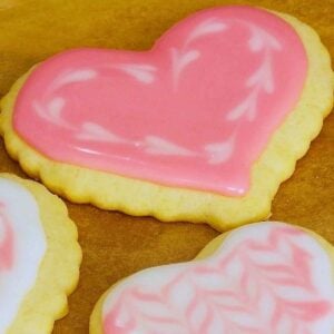 Two heart shaped sugar cookies with pink and white marbled icing on a parchment paper background.