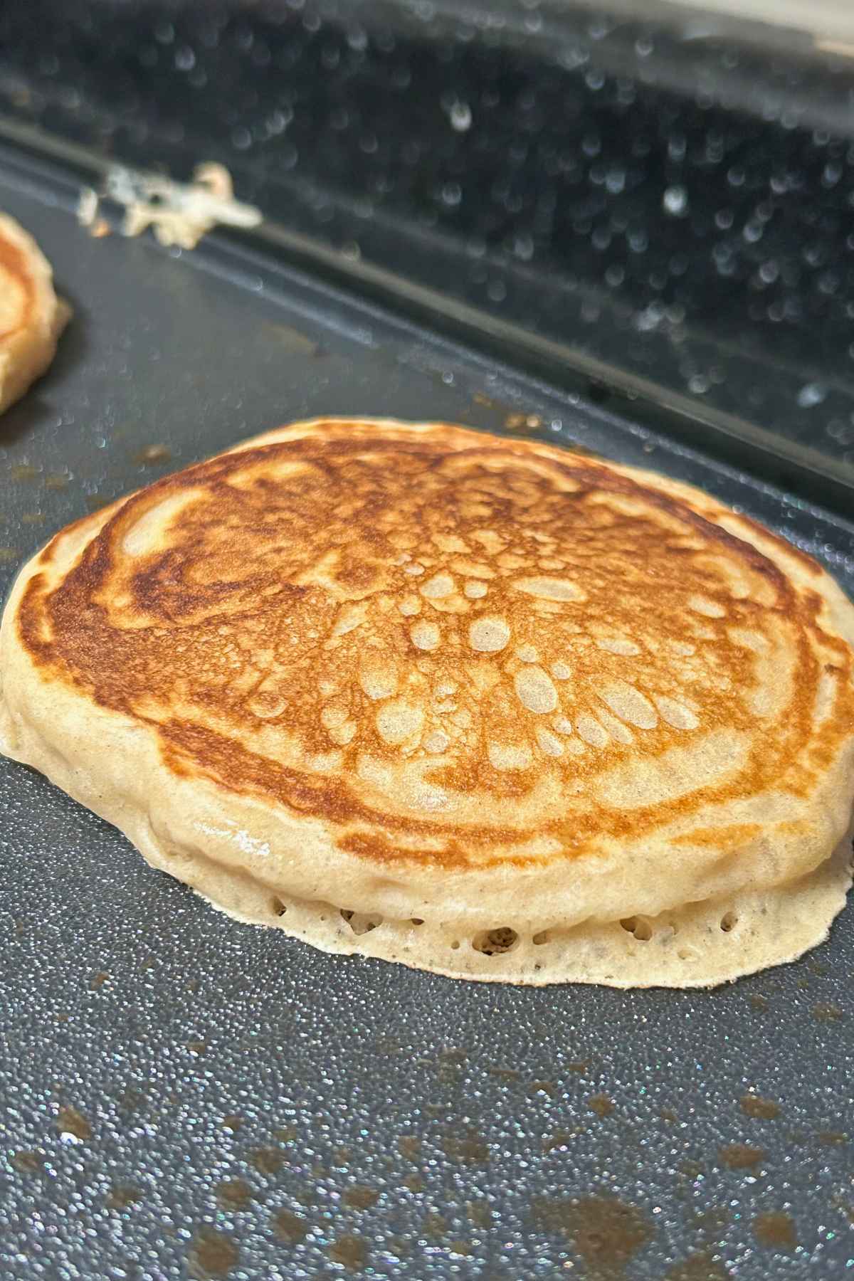 Up close image of one golden brown buttermilk pancake cooking on a griddle, showing the perfectly fluffy texture and toasted surface.