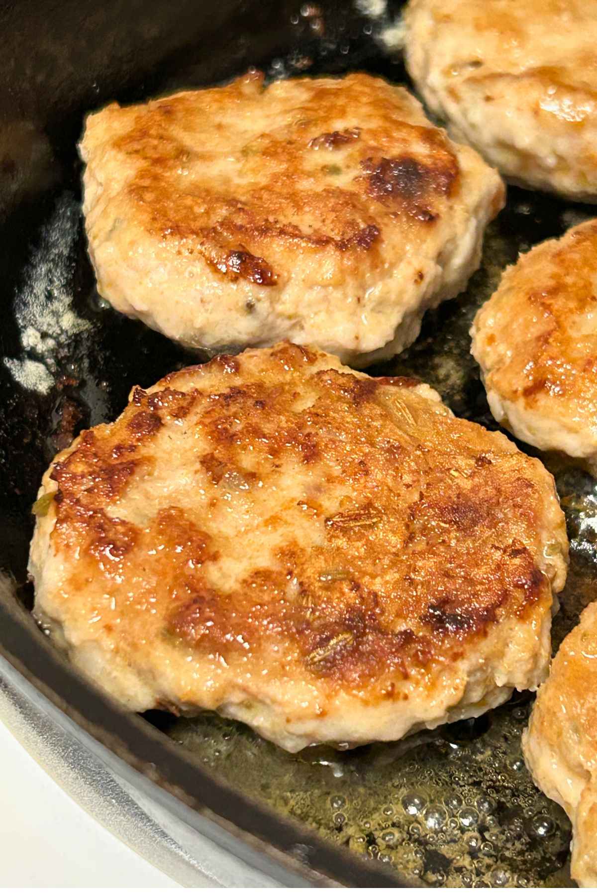 Close-up of Chicken Breakfast Sausage patties cooking until crispy and browned in a pan.