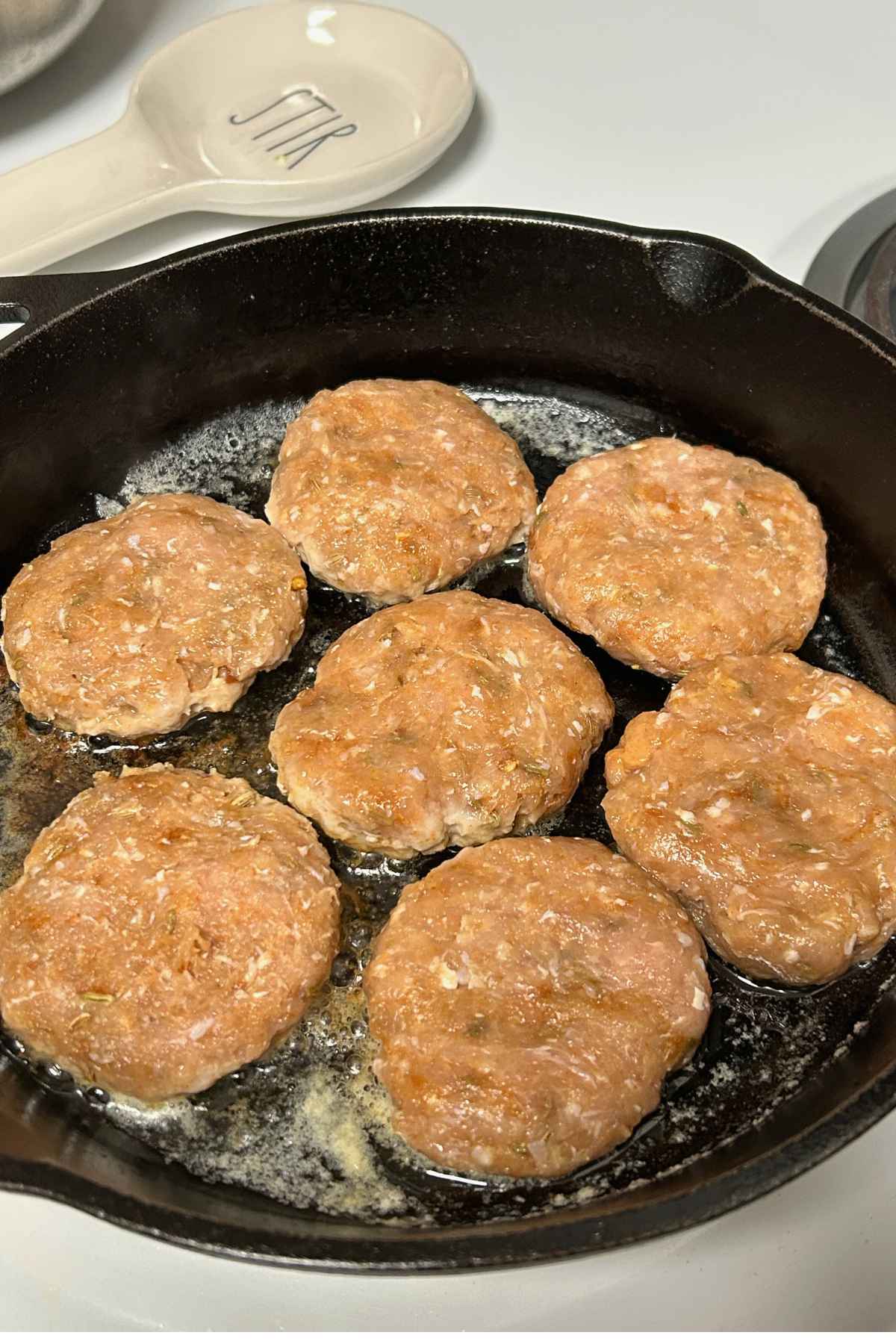 Six raw ground poultry patties arranged in a black cast iron skillet cooking in butter.