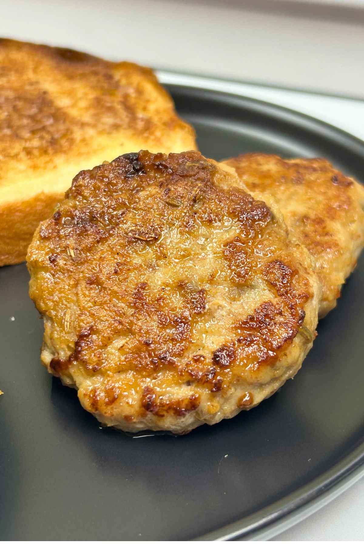 A close-up of cooked chicken breakfast sausage patties with a side of buttered toast.