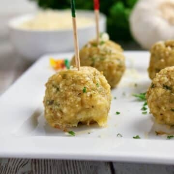 Chicken Parmesan Meatballs served on a white platter, with a toothpick inserted into the front meatball.