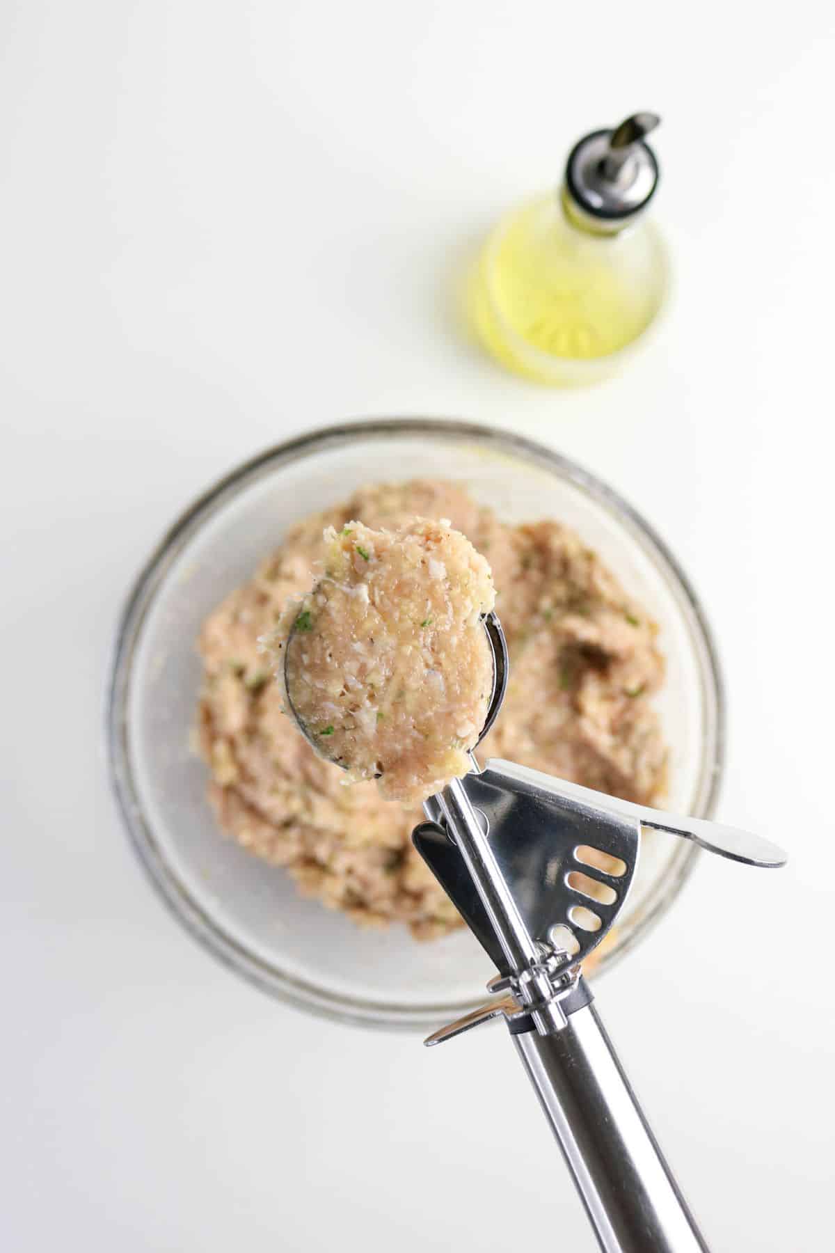 Scooping ground meat mixture out of a clear bowl to shap into uniform rounds.