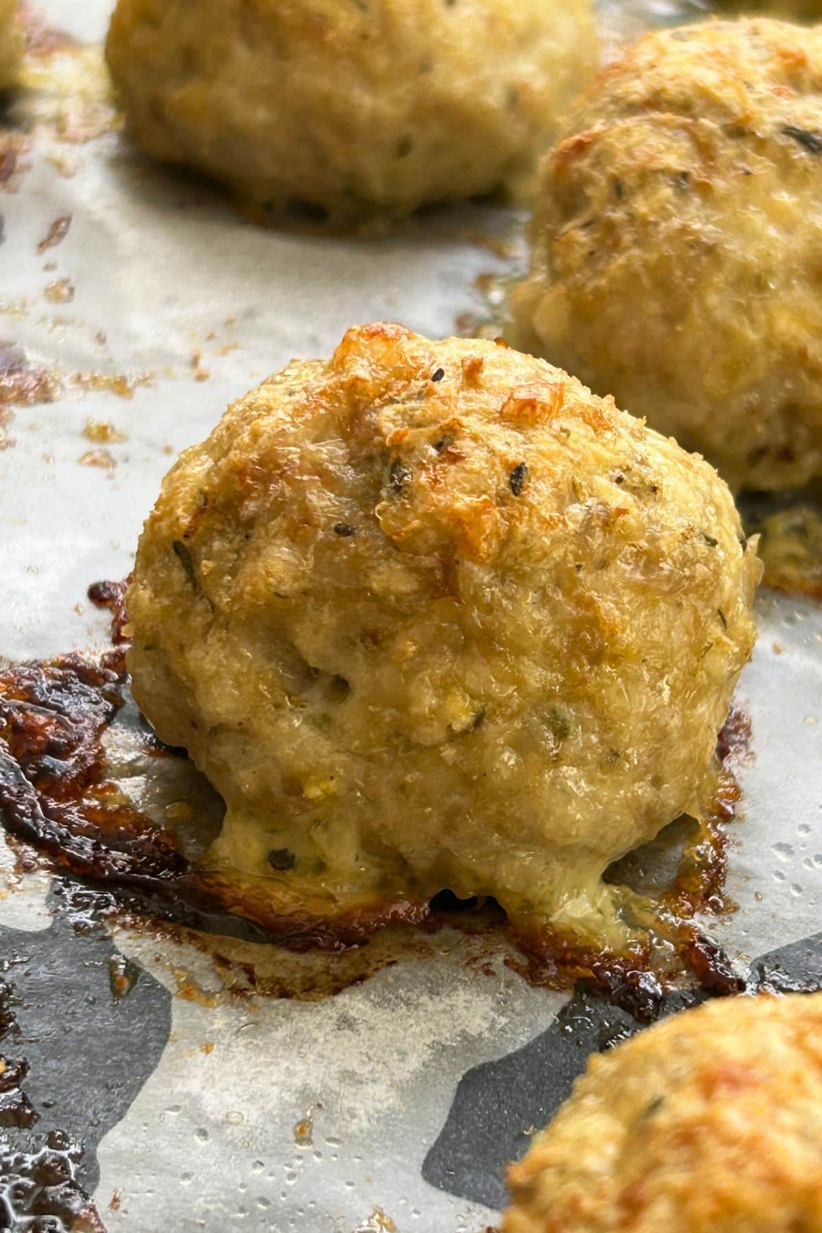 Close up of a golden, baked meatball fresh out of the oven on a parchment paper lined baking sheet.