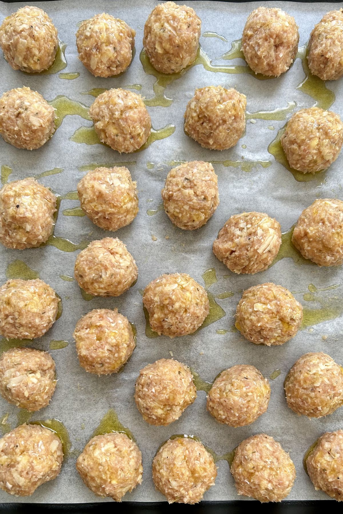 Raw meatball mixture arranged on baking paper and drizzled with olive oil before cooking