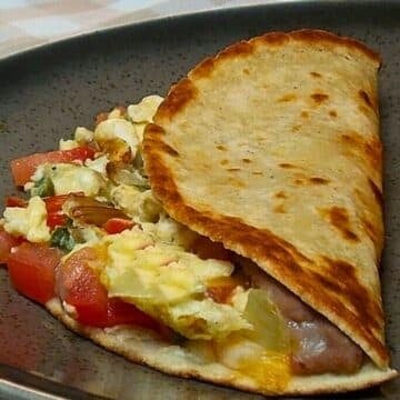 Scrambled egg and vegetable breakfast wrap served on a dark speckled plate.