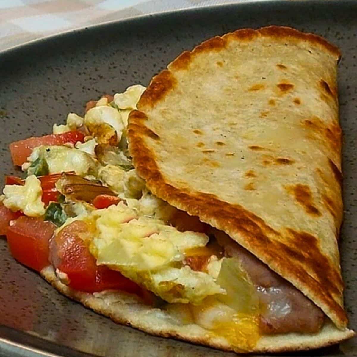 Scrambled egg and vegetable breakfast wrap served on a dark speckled plate.
