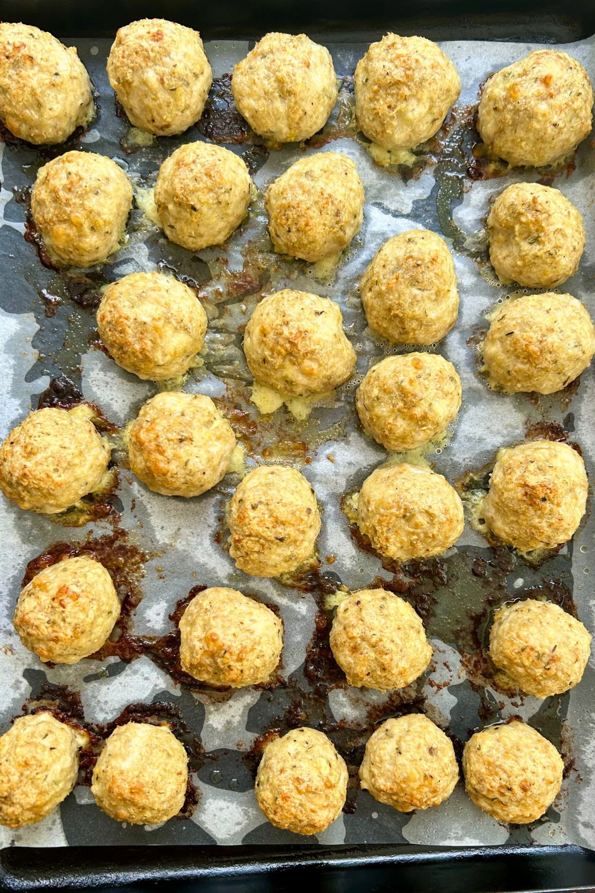 Baked Chicken Parmesan Meatballs lined up on a parchment covered baking sheet.
