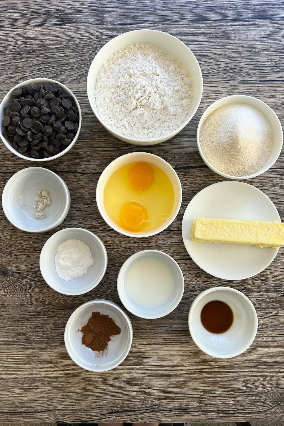 Overhead view of baking ingredients measured into white bowls on a wooden background.
