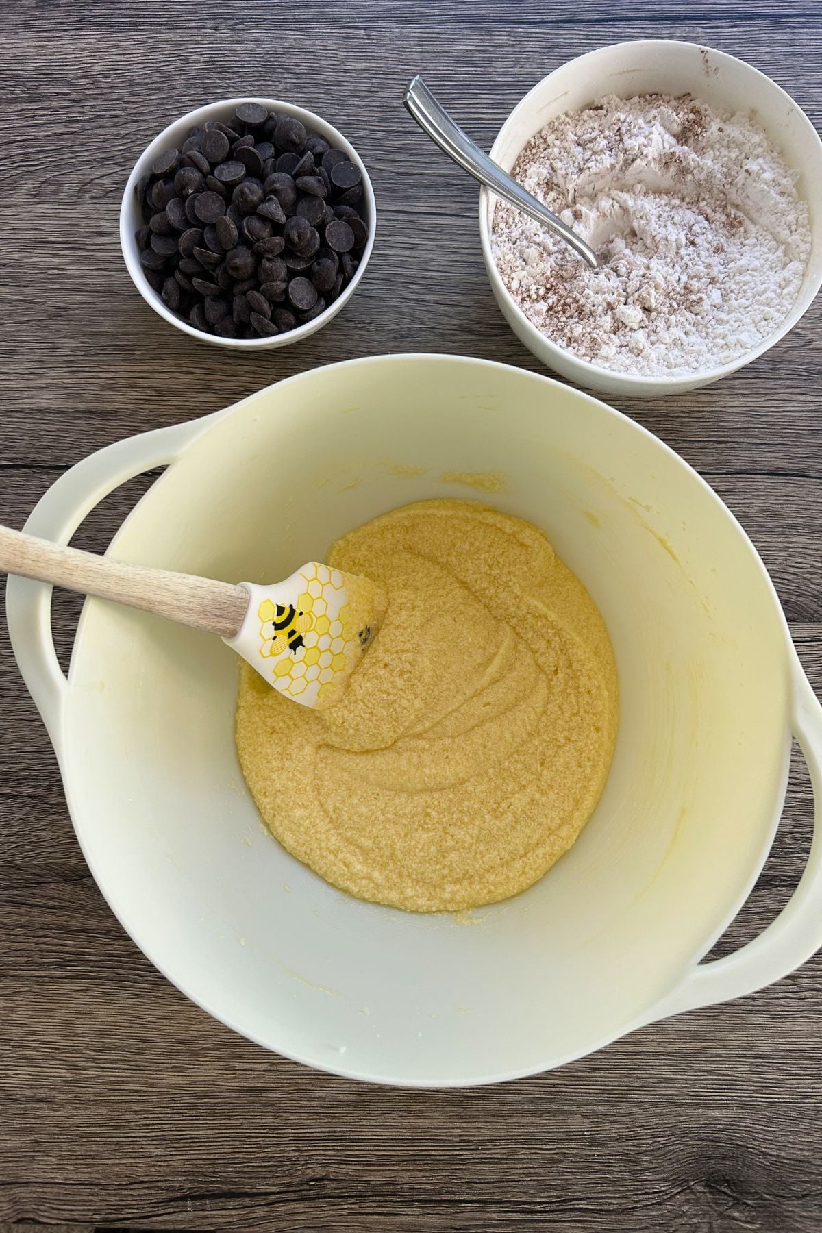 Creamed butter mixture in a large bowl alongside separate bowls of chocolate chips and flour mixture.