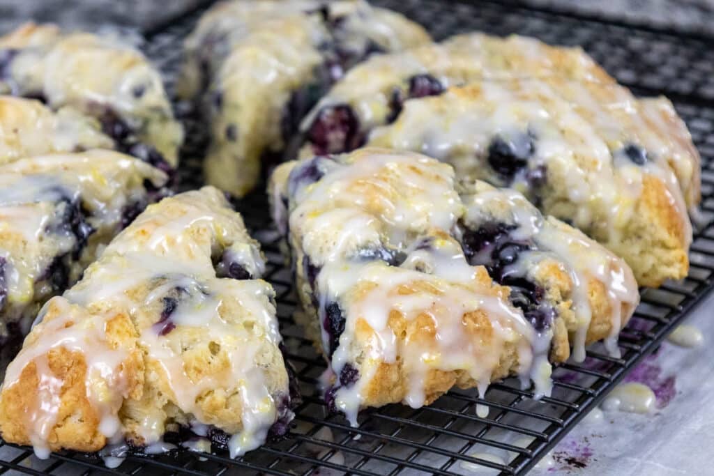 Freshly bake golden brown scones topped with a sweet lemon icing, arranged on a black wire cooling rack.