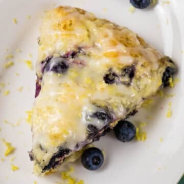 Overhead image of a blueberry scone with lemon glaze, sprinkled with lemon zest on a white plate.
