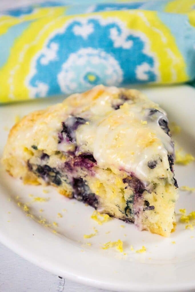 A wedge-shaped pastry packed with dark purple berries, topped with white icing and fine yellow zest, sitting on a white plate.
