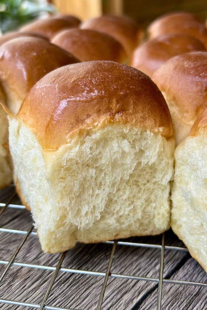 Freshly baked sweet dinner rolls on a wire cooling rack, highlighting a soft, pulled-apart roll.