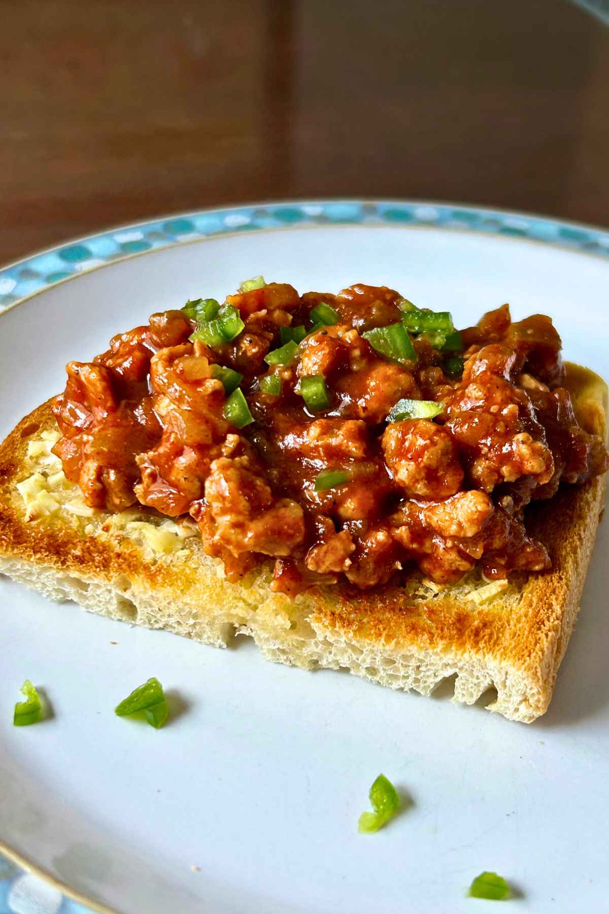 A hearty scoop of savory venison sloppy joe meat served open-faced on thick toasted bread, garnished with fresh, finely chopped green peppers on a white plate.