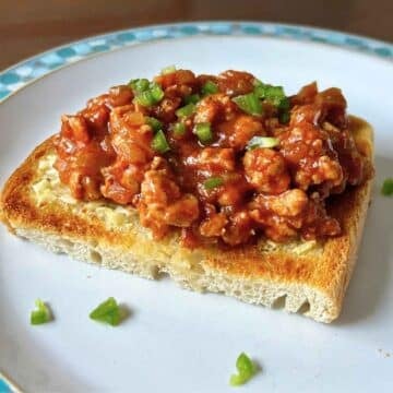 A hearty scoop of savory venison sloppy joe meat served open-faced on thick toasted bread, garnished with fresh, finely chopped green peppers on a white plate.
