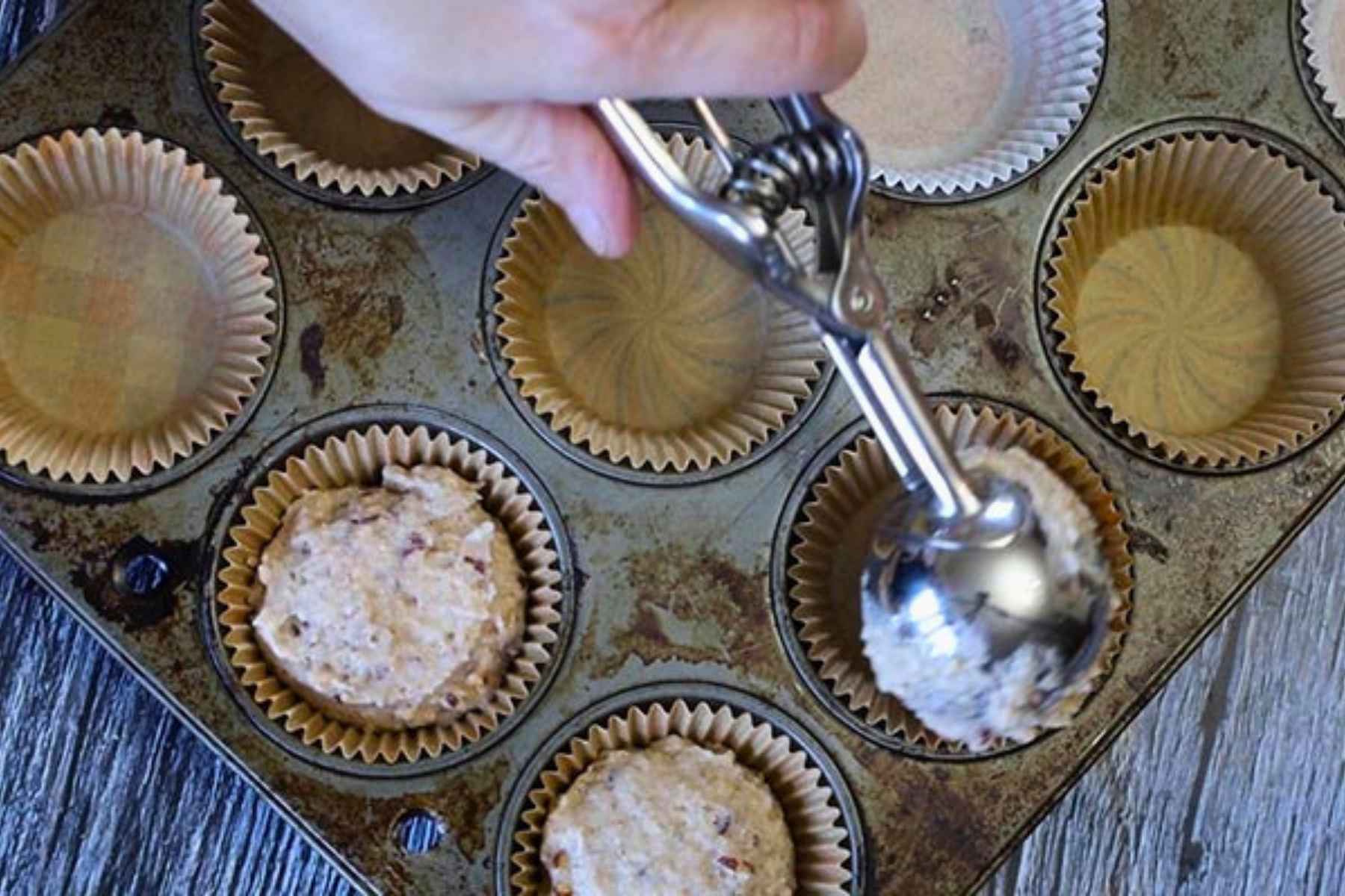 A hand scooping muffin batter into a paper liner.