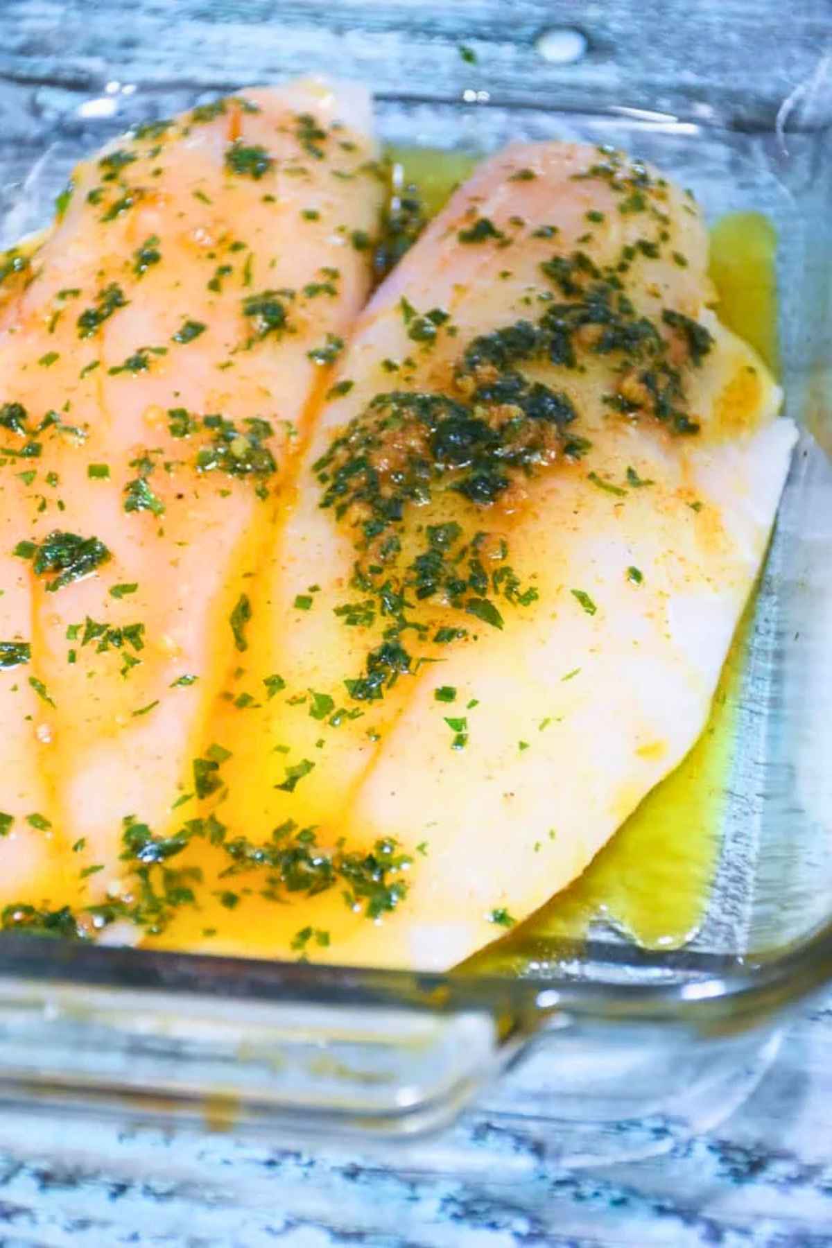 Raw red snapper fillets coated in melted butter and parsley in a baking dish.