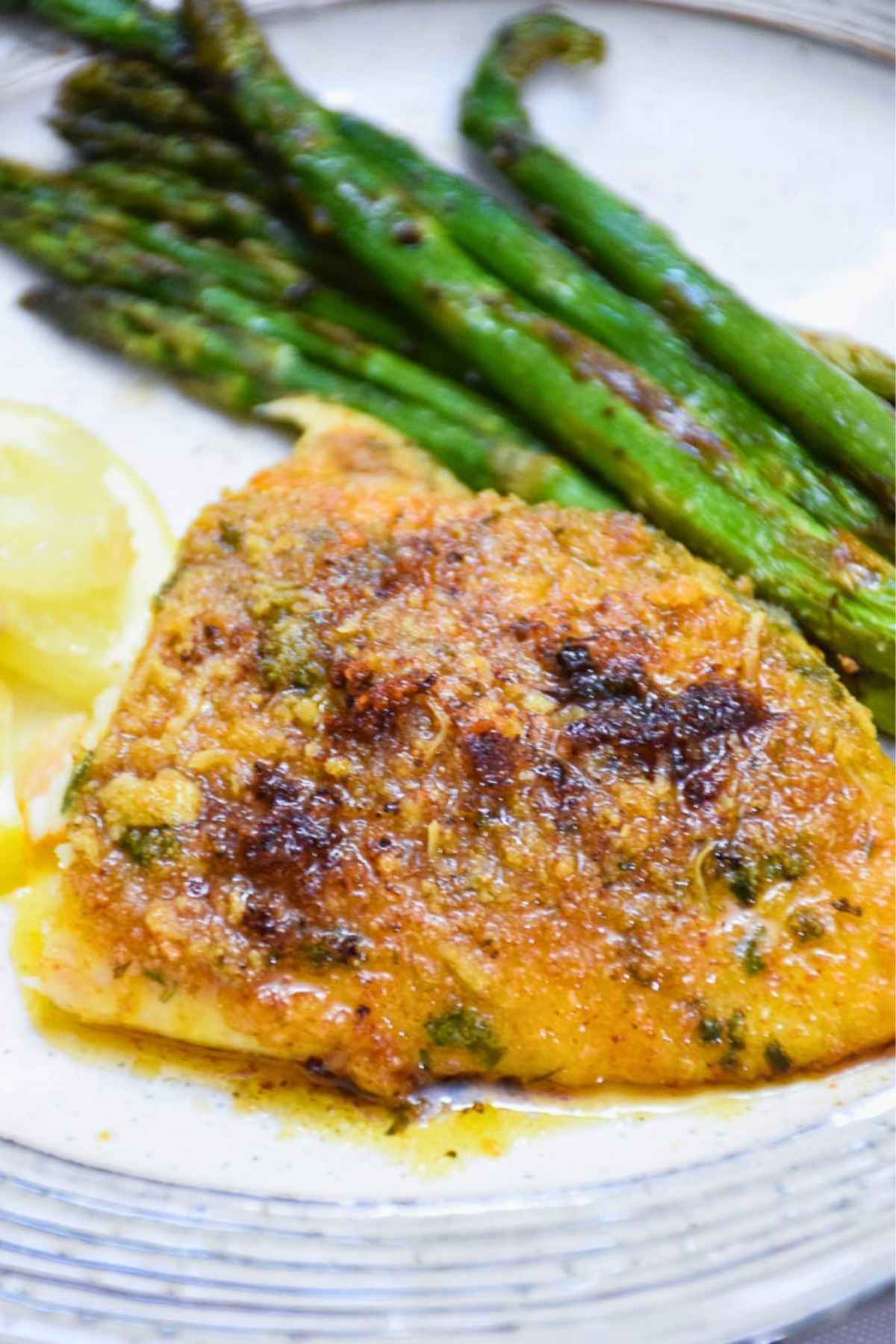 Baked red snapper fillet served with roasted asparagus on a white plate.