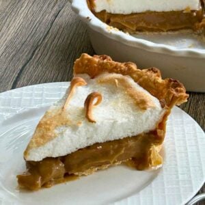 A slice of homemade butterscotch meringue pie on a white plate with the whole pie in the background.