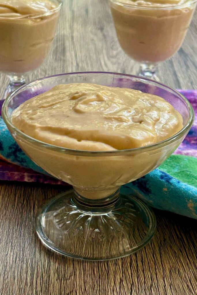 Clear glass footed dish filled with creamy pudding resting on a colorful tea towel.