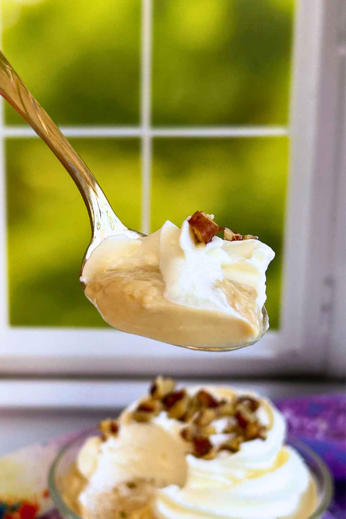 Close-up of a silver spoon holding a bite of creamy pudding topped with whipped cream and chopped pecans.