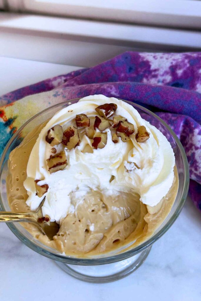 Top-down view of creamy dessert in a glass dish with swirled whipped cream and chopped pecans.