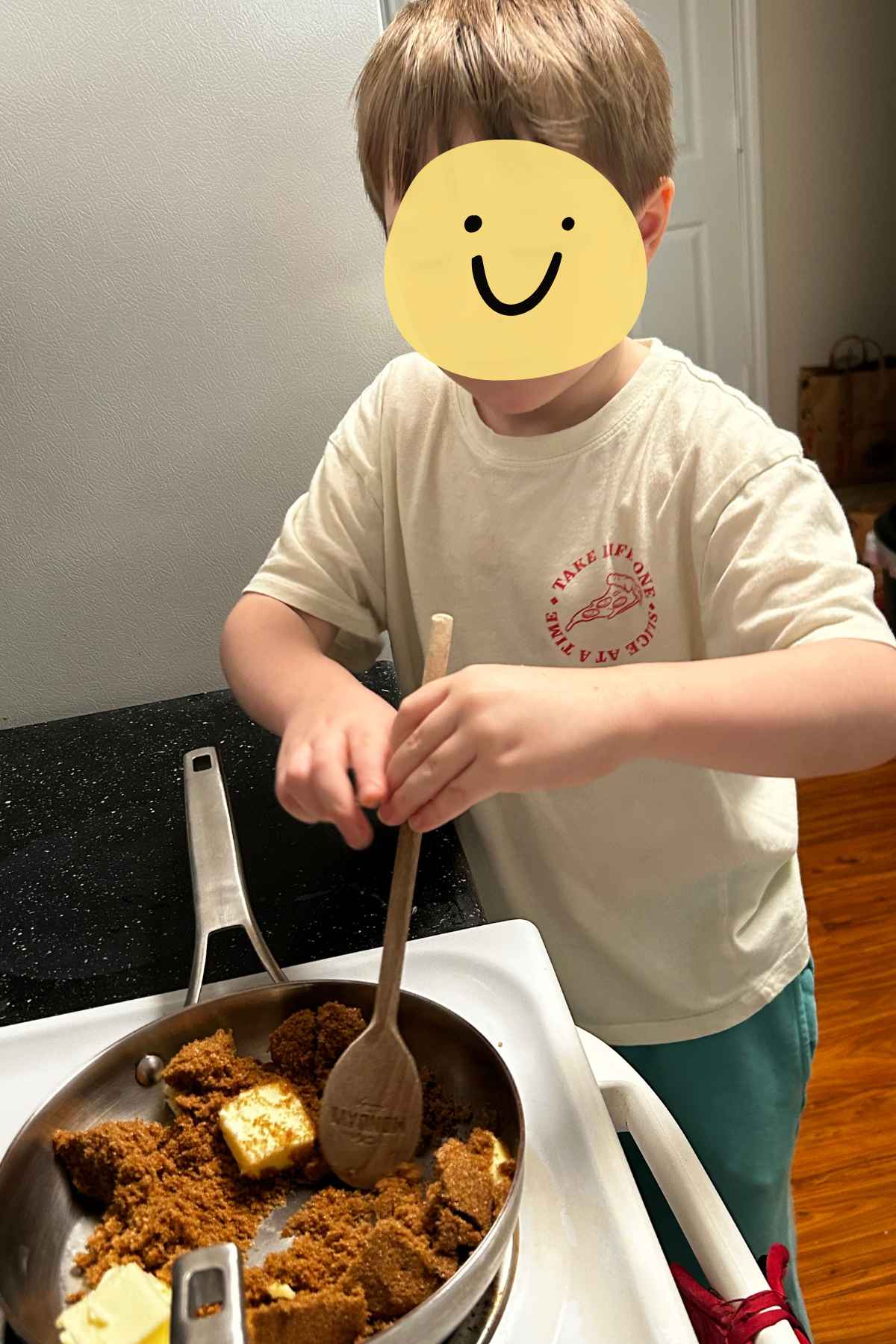 My grandson stirring dark brown sugar and butter together over low heat on an electric stove.