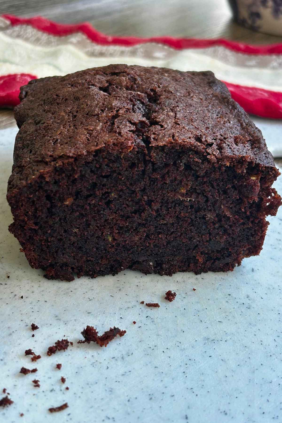 A sliced loaf of rich double chocolate zucchini bread showing its moist texture with a few crumbs scattered in front.