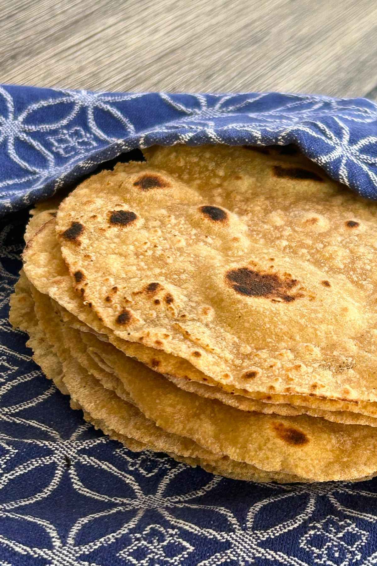 A stack of thick, golden-brown homemade corn and flour tortillas wrapped inside a blue and white patterned cloth napkin.