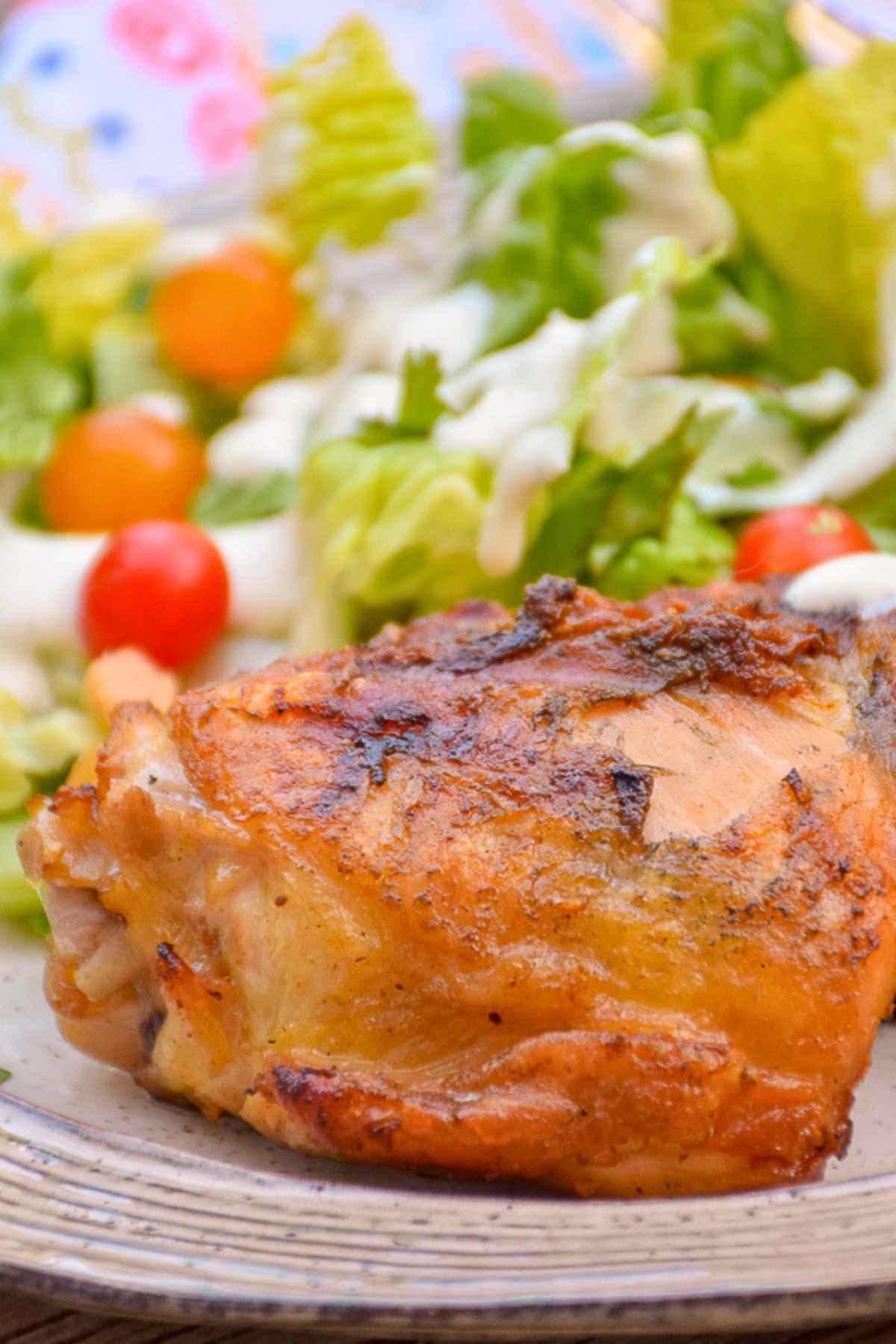 Golden-brown fireman's bbq grilled chicken thigh on a plate with a fresh green side salad.