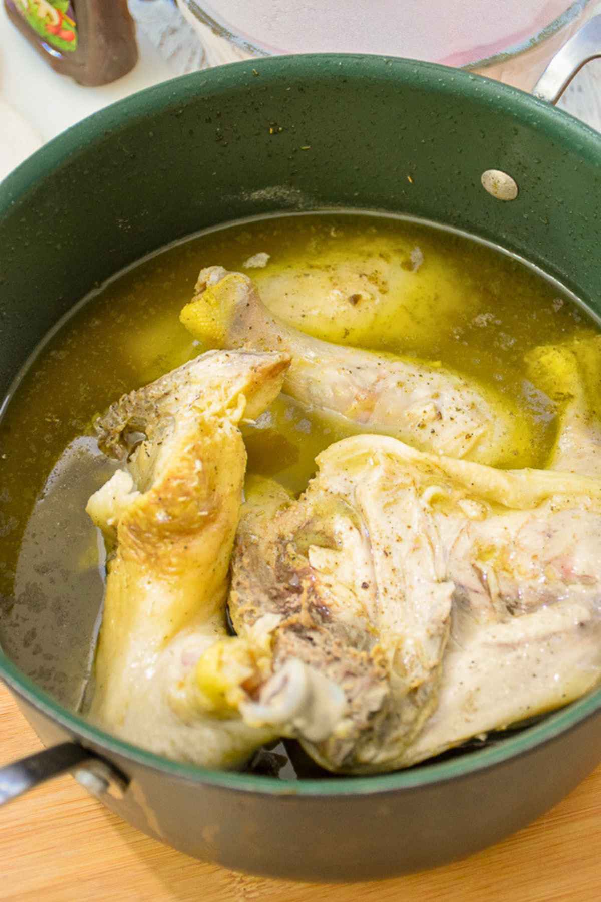 Parboiled chicken quarters in a large green stockpot.