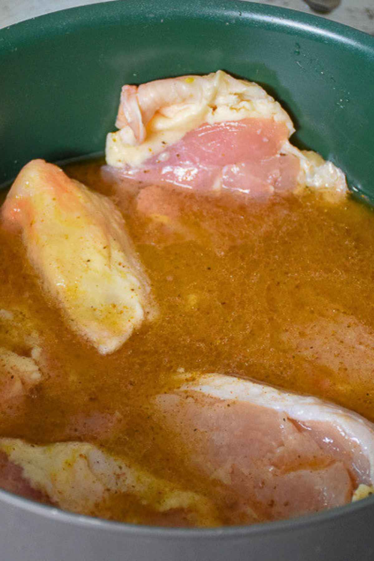Raw chicken pieces soaking in a pot filled with liquid marinade.