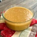 Glass bowl of smooth, golden homemade whipped maple butter sitting on a red patterned towel.