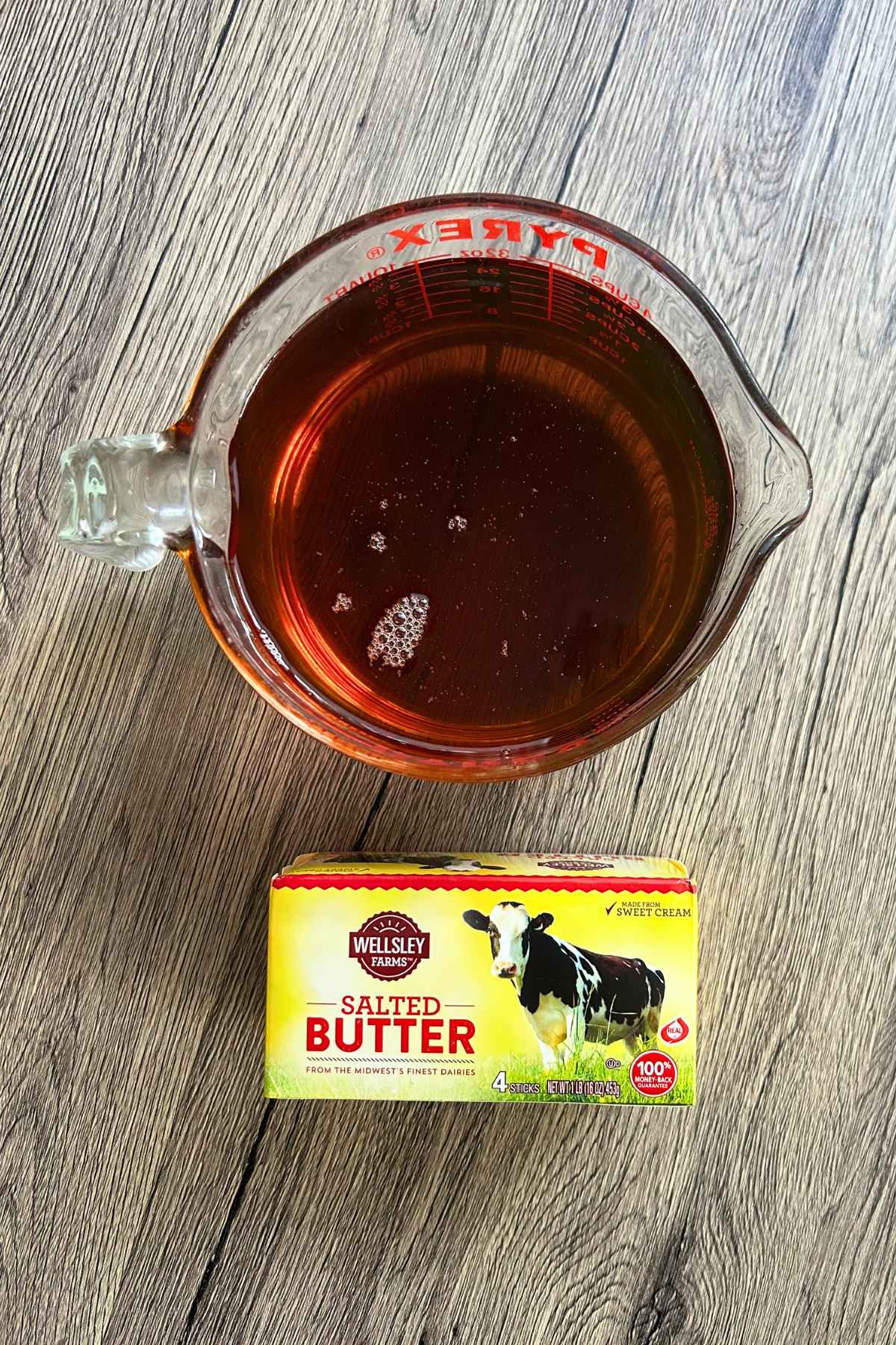 Glass measuring cup of pure Grade A maple syrup next to salted butter on light wood.