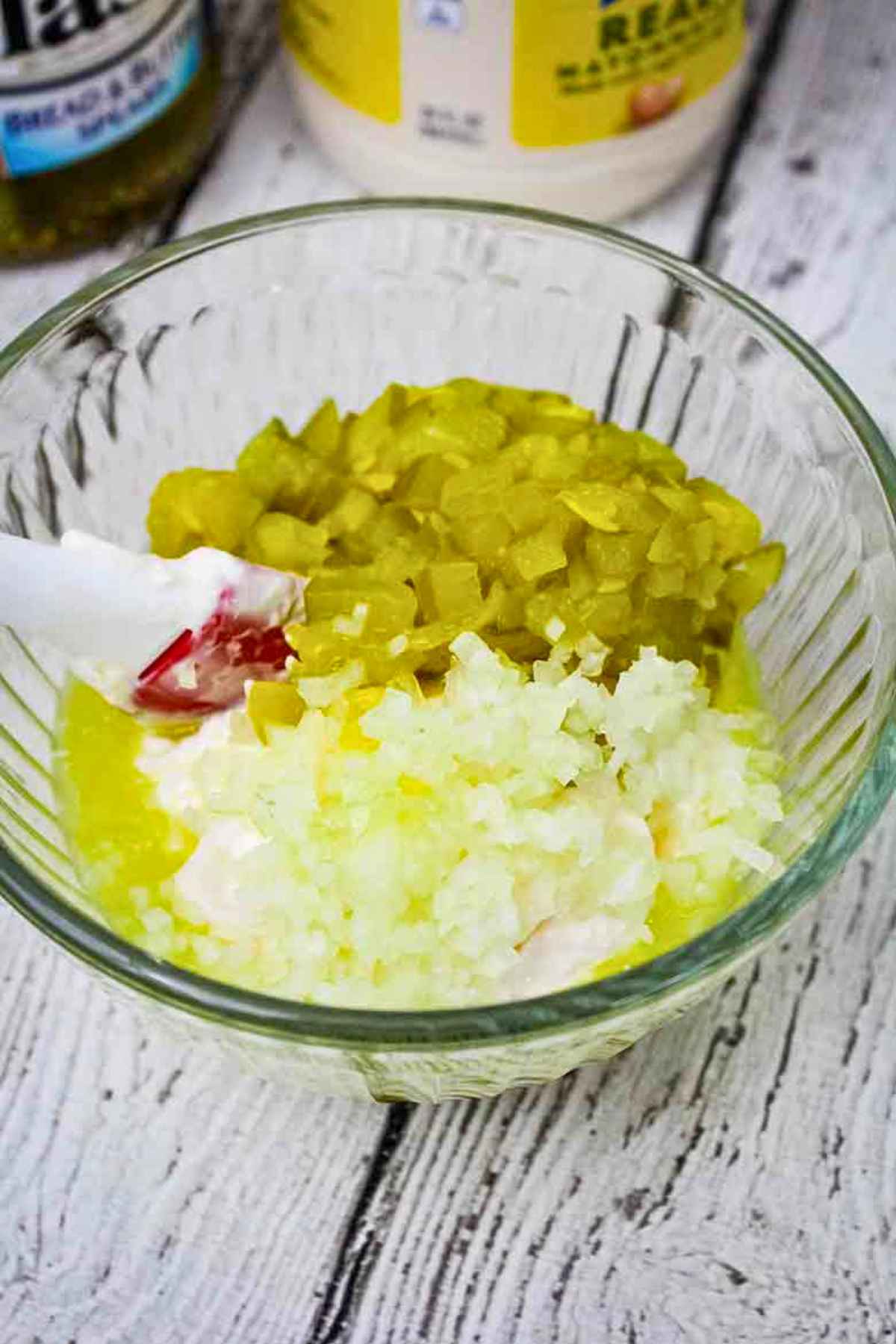 Finely diced pickles, minced onions, and mayonnaise in a small glass bowl ready to be mixed together.