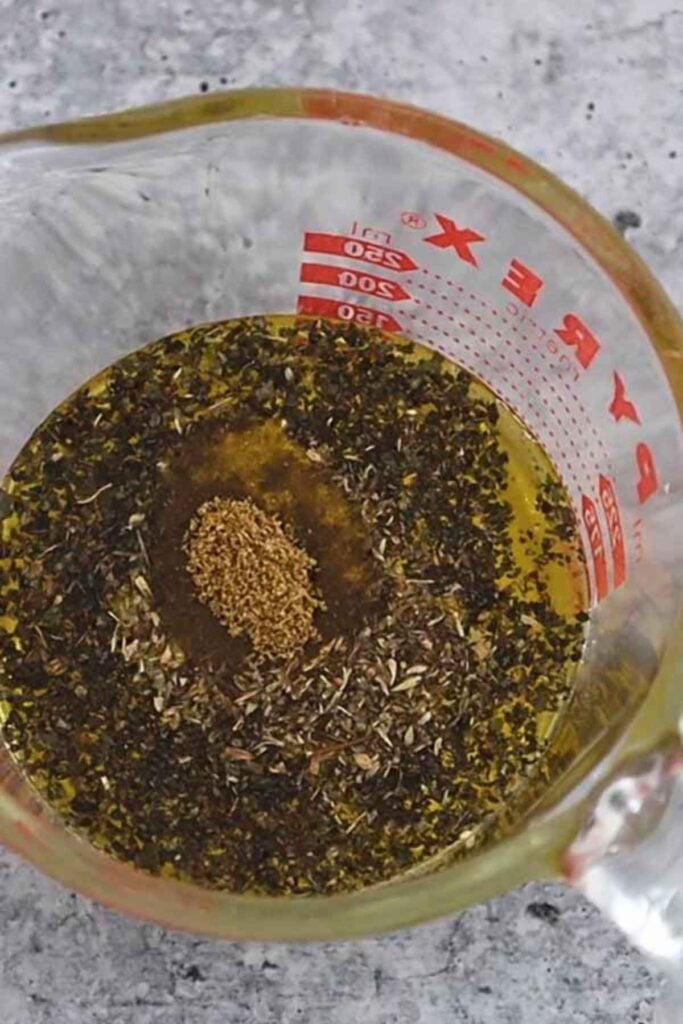 An overhead view of oil and mixed herbs sitting inside a glass pyrex measuring cup.