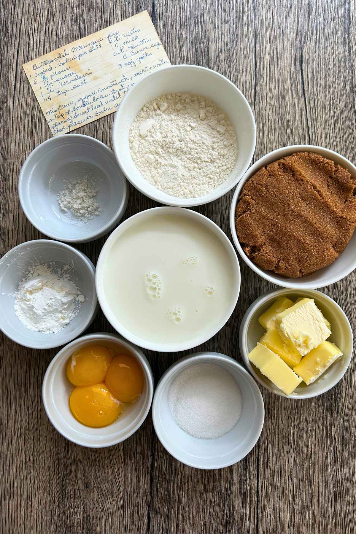 Overhead view of measured ingredients in white bowls next to a handwritten recipe card.