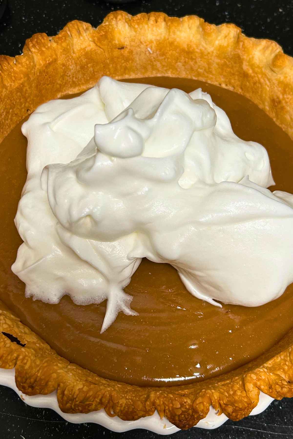 Whipped egg whites on top of warm butterscotch pie ready to be spread out over top of the pie.