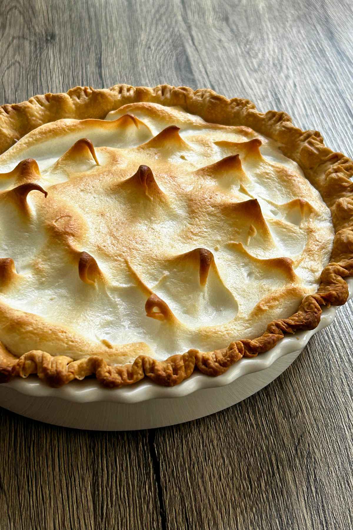 A whole butterscotch pie with golden meringue topping cooling on a wooden table.