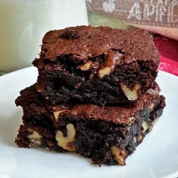 Two thick, fudgy walnut brownies stacked on a white plate with large walnut pieces visible.