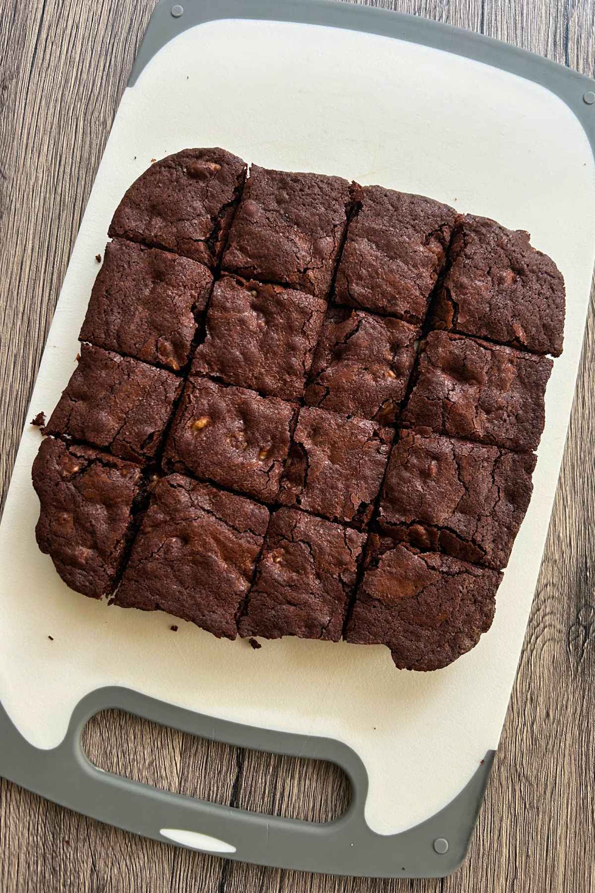 Top-down view of a slab of baked walnut brownies cut into square pieces on a white cutting board.