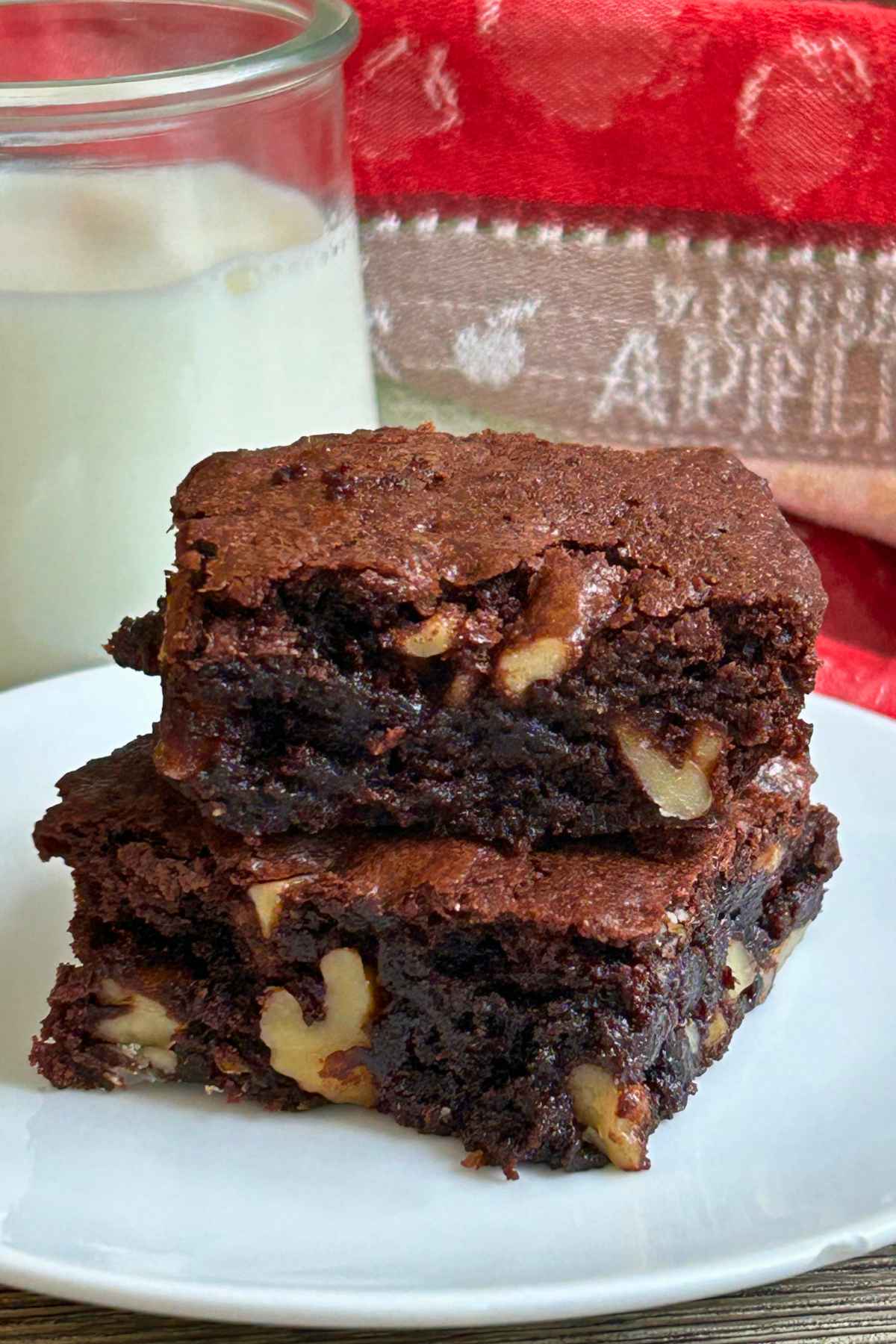 Two thick, fudgy walnut brownies stacked on a white plate with large walnut pieces visible.