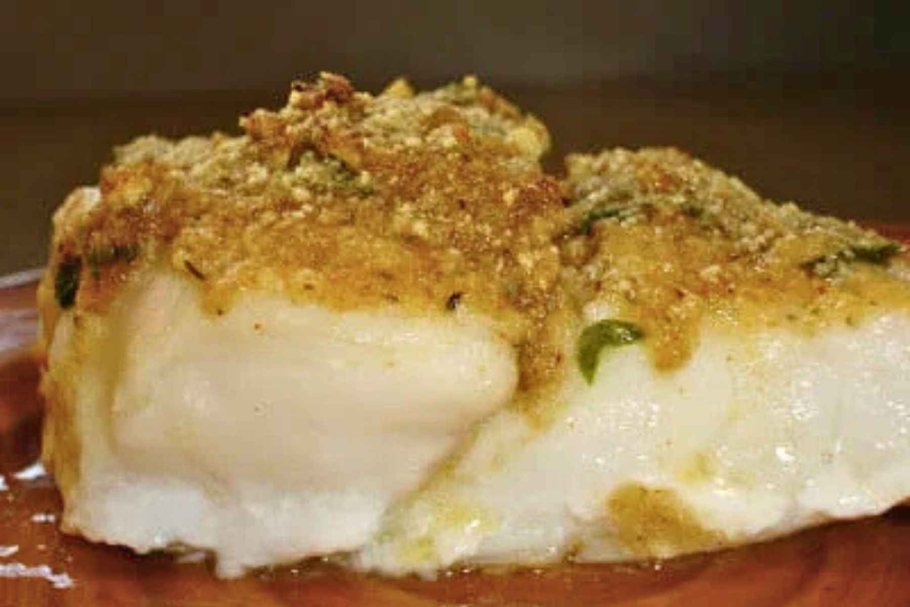 Side view of a thick, flakey white fish fillet topped with a golden-brown herb and breadcrumb crust.