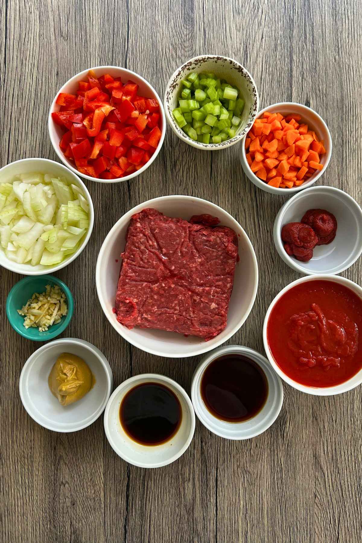 An overhead shot of prepped ingredients in small bowls, including raw ground beef, chopped vegetables, sauces, and seasonings.